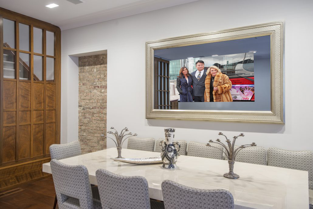 gold reflectel mirror tv hangs on white wall over dining room table
