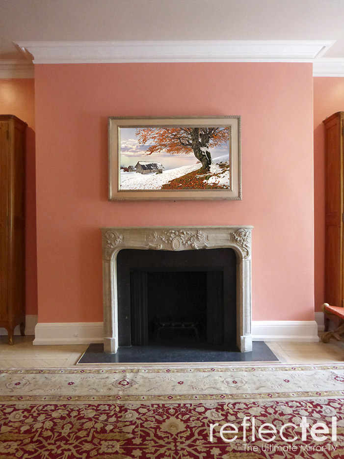 gold reflectel mirror tv hangs over stone mantle on peach wall