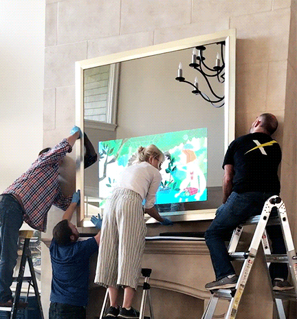 Two Men and 1 Woman Installing a Reflectel Mirror TV over stone mantle