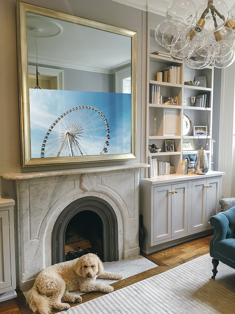 Portrait Orientation Mirror TV With Gilded Shaped Frame Over A Marble Mantel Turned On In Brooklyn Townhouse NYC With Dog
