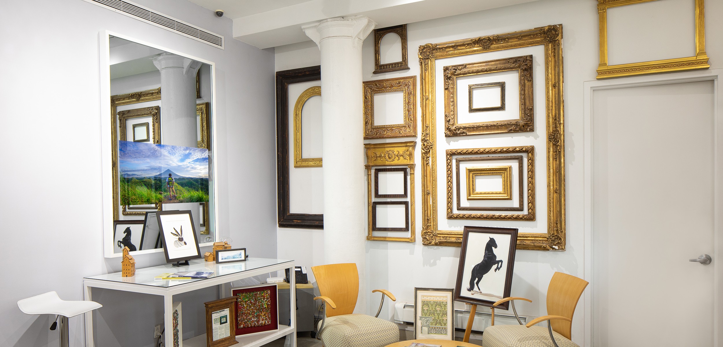 Showroom with numerous gold carved frames on white wall and photo of horse on easle, White Framed Mirror TV on left wall