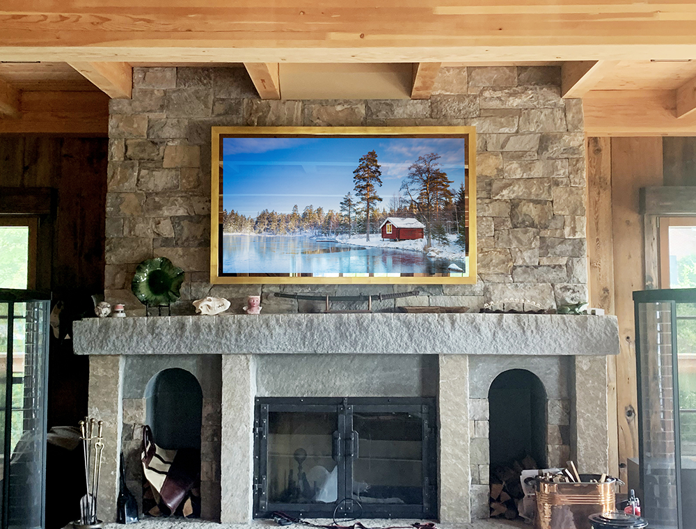 Gold Framed Tv With Plus Size Glass And Wood Buildup Over Fireplace In Living Room
