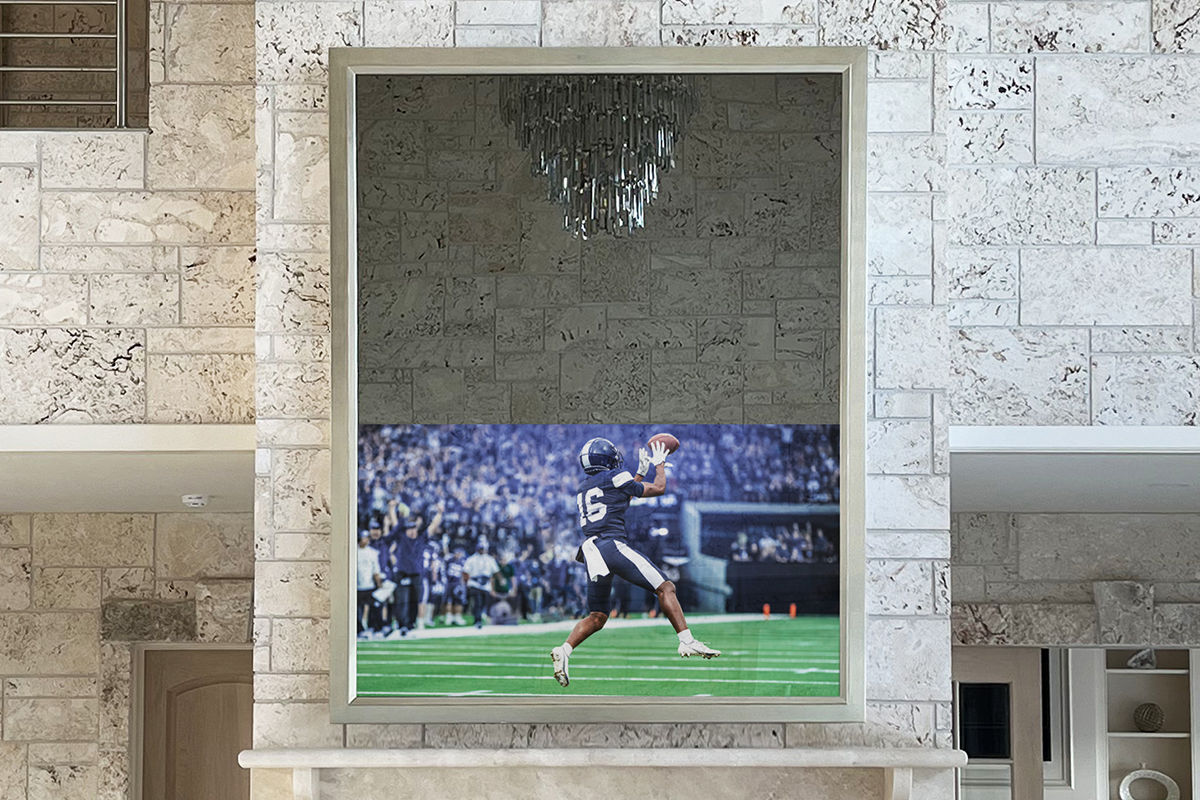 Tall Silver Mirrored Television Over A Fireplace