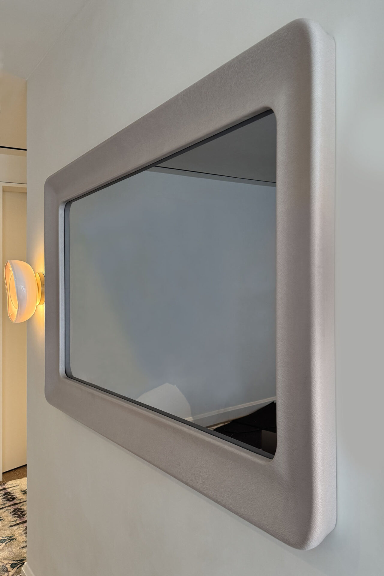 Recessed Mirror TV With A Rounded Blush Colored Leather Frame On White Wall