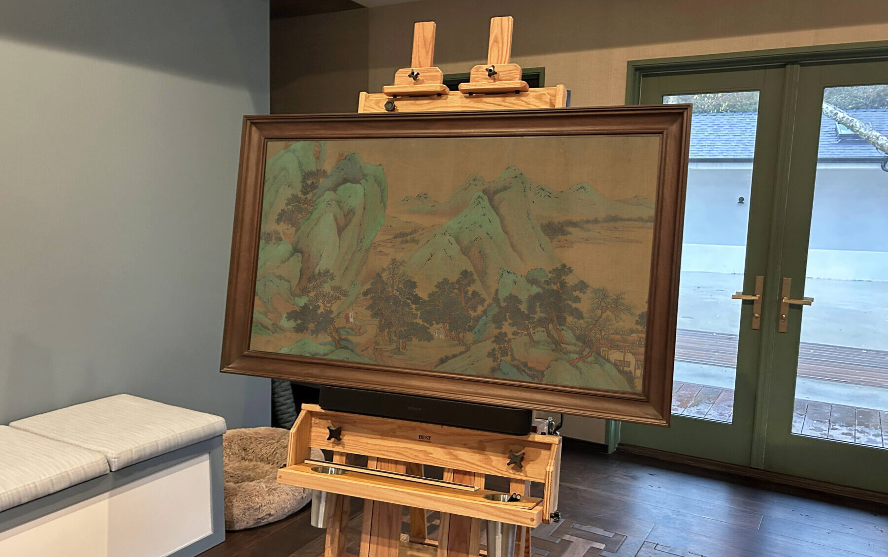 art display on tv frame mounted on easel in sitting room with doors leading outside