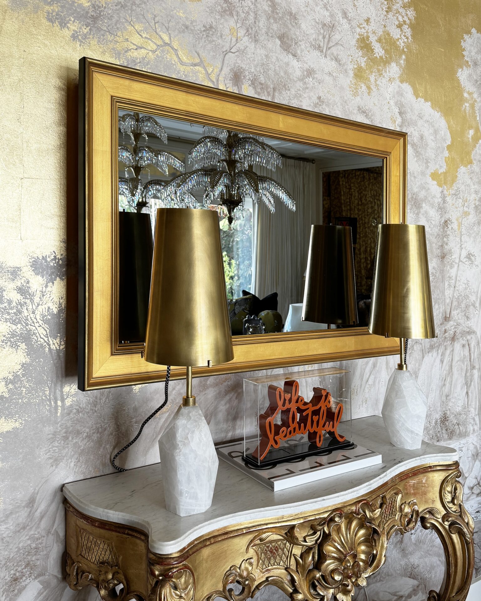 mirror tv with gold frame in the kips bay decorator show house in lori morris design's gilded palm room over a baroque gold console with two gold lamps in a luxury designer room