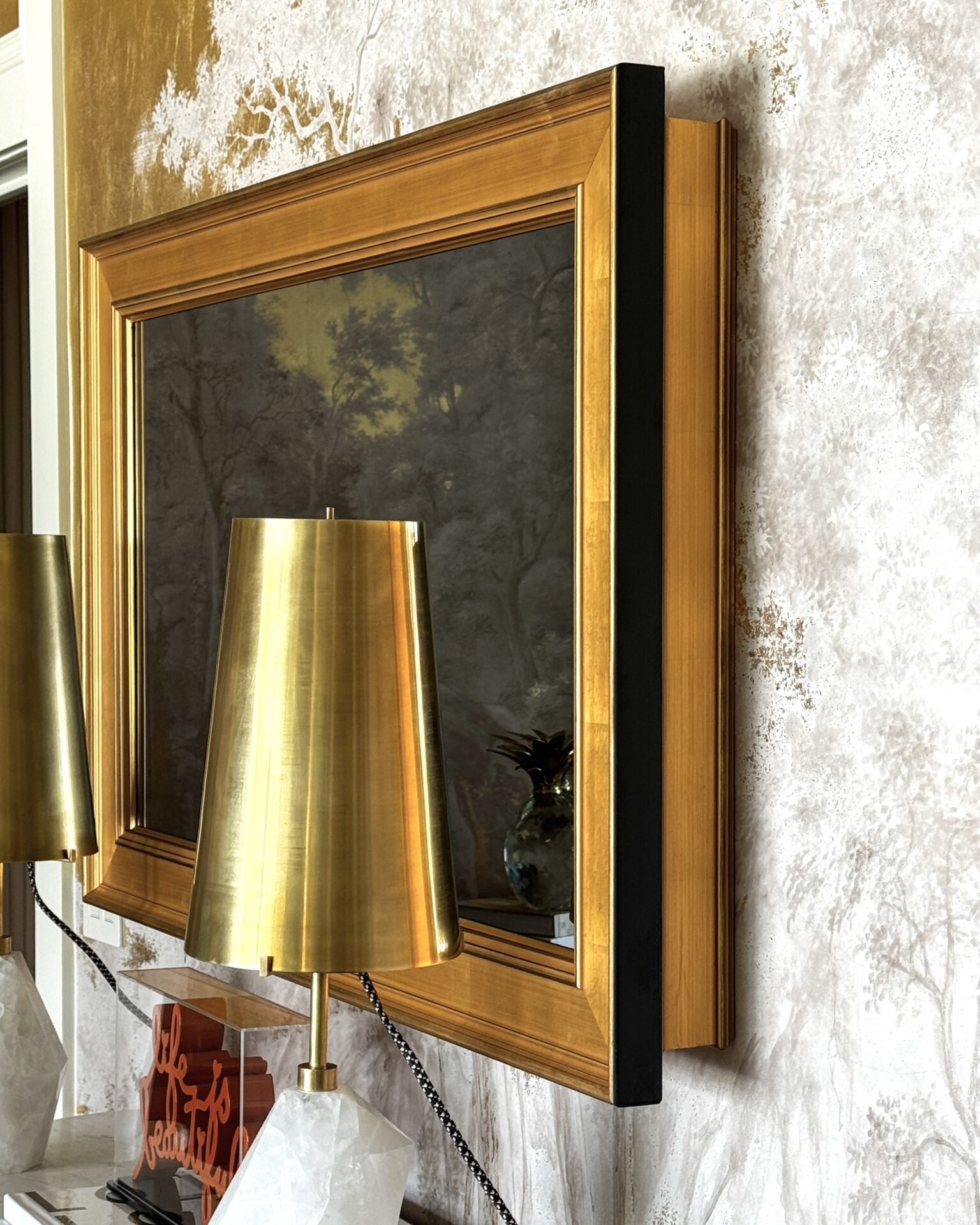 side shot of gilded shaped framed tv hiding tv sides in designer room by lori morris design at kips bay show house with gold lamps in front of the gold mirror tv