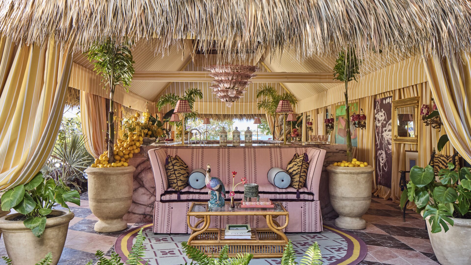 kips bay show house palm beach 2026 river brook interiors tiki tent with custom gold tv mirror in cabana with pink couch, gallery walls, outdoor space, outdoor curtains, and outdoor bar space