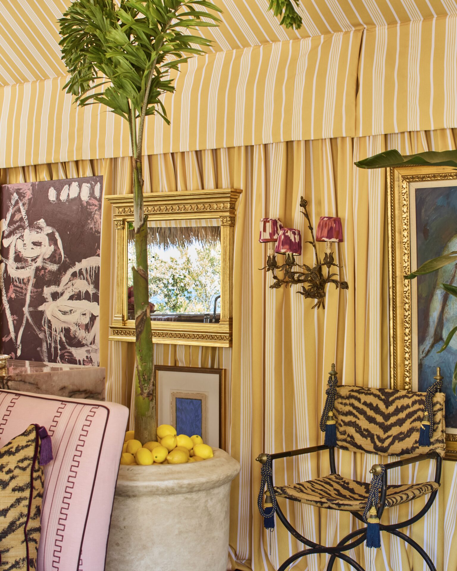 tabernacle gilded carved framed tv mirror in river brook interiors tiki tent at the kips bay decorator show house palm beach against yellow striped curtains, art, palm trees, and a zebra chair with hidden tv mirror off