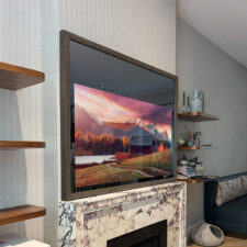 Square shaped mirror tv with brown wood frame over matble fireplace mantel