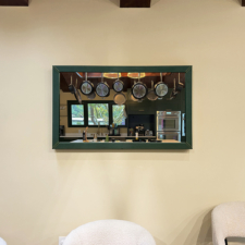 50" Landscape - Leather Green framed mirror tv hung on wall reflecting the kitchen behind it.