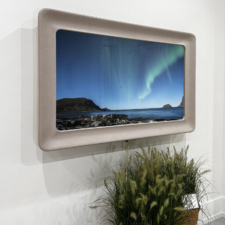 55" Rounded Corner - Cortina Leathers: Hampton Designer Show House 2025 grey leather swoop framearound mirror television turned on with northern lights image playing above planted pots in showroom
