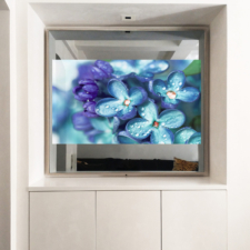 55" Square Plus - Metal Mirror tv with silver frame turned on over a media light colored cabinet.