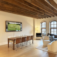 65" Rounded Corner - Leather Rounded corner hidden mirror TV turned on inside open concept dining living space.