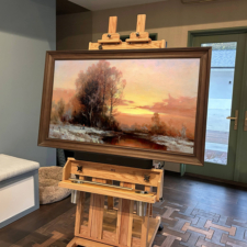 55" Landscape Framed TV - Mahogany Wood install on an easel Framed television turned on resting on easel by windowed doors leading outside.