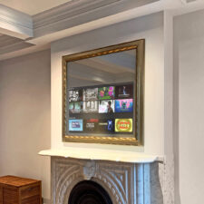 49" Square Plus - Gilded Carved (GC24) Golden framed mirror television turned on over fireplace mantel.