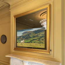 43" Square Plus - Signature Shaped (SS9-G-O) Gold wooden framed Reflectel mirror TV over marble mantle in yellow toned paneled room.