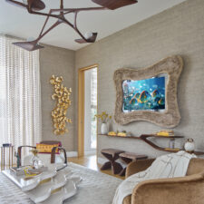 49″ Serpentine - Schumacher Faux Fur: Holiday House Hamptons 2025 A-symmetrical fur-framed mirror television turned on in living room showroom