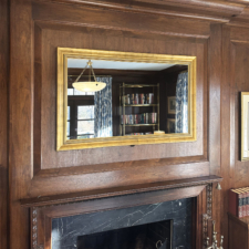 50" Landscape - Signature Shaped (SS16-G-O) Mirror TV with a gold wood frame installed in a recess in a library