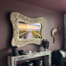 49″ Serpentine - Schumacher Faux Fur - Hannah Brooke Design - Holiday House Wellington Serpentine shaped Mirror TV with a Schumacher faux fur frame over a marble credenza in bedroom for Holiday House Wellington